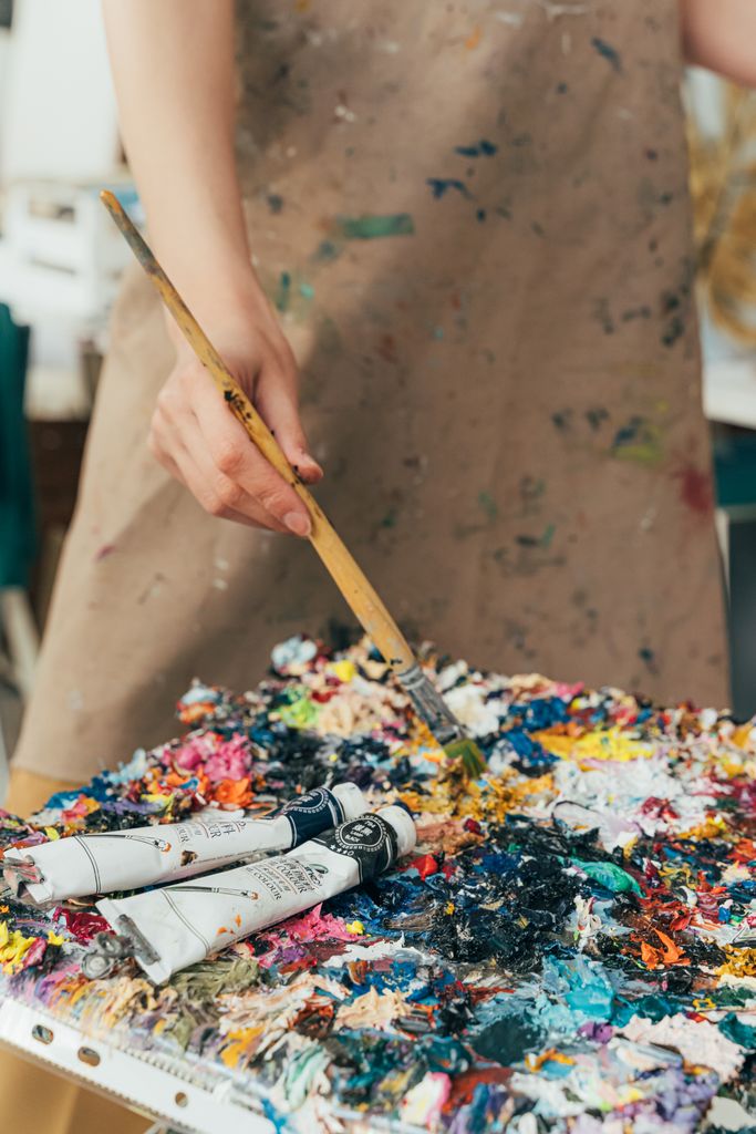 Close-up of an artist mixing vibrant colors on a messy palette in an art studio.